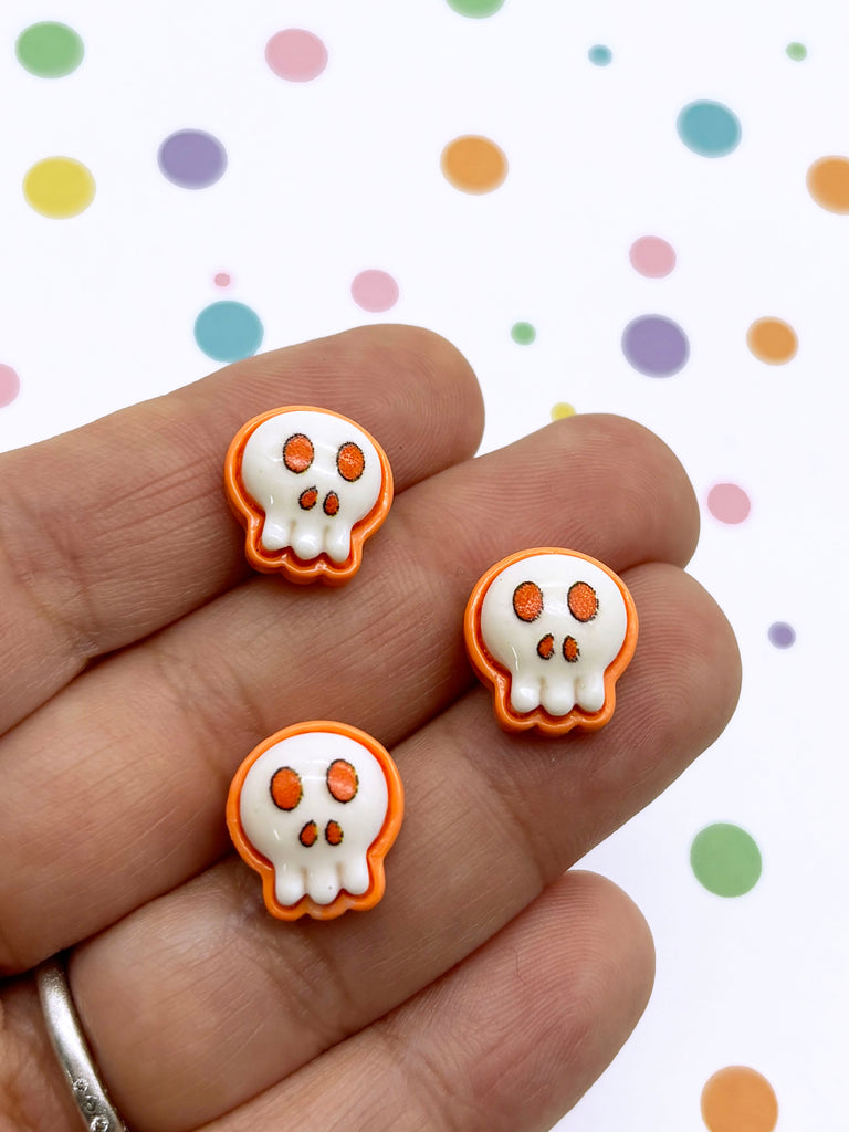 a hand holding three small orange and white skulls