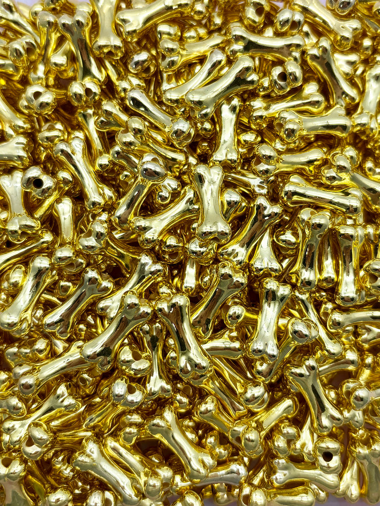 The image is a close-up of numerous small, shiny gold-colored metal objects, such as small bones or beads, arranged in a visually striking and intricate pattern.