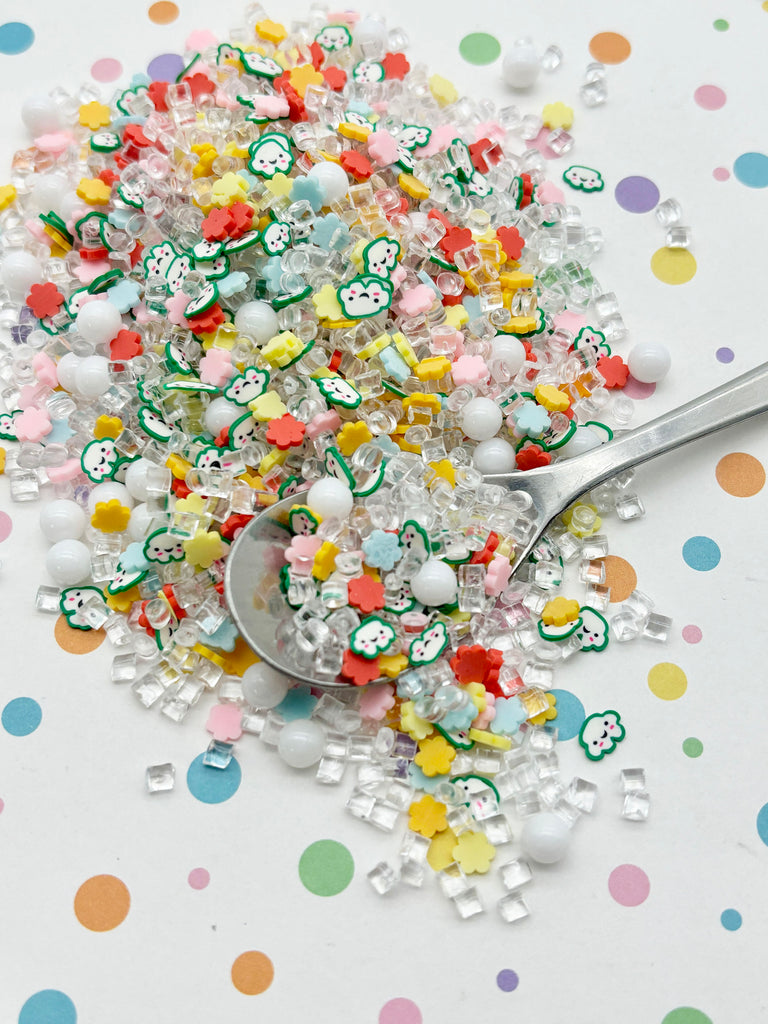 a pile of colorful, multicolored candy pieces scattered on a surface with polka dots. A spoon is visible among the candy pieces, suggesting it may be used to scoop up the candy.