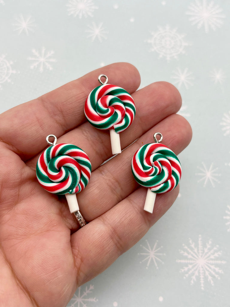 A hand holding three colorful candy lollipops against a snowy background.
