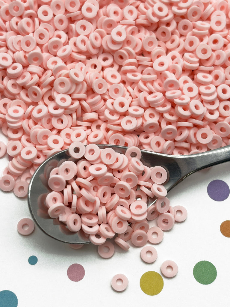 a spoon full of pink beads next to a polka dot background