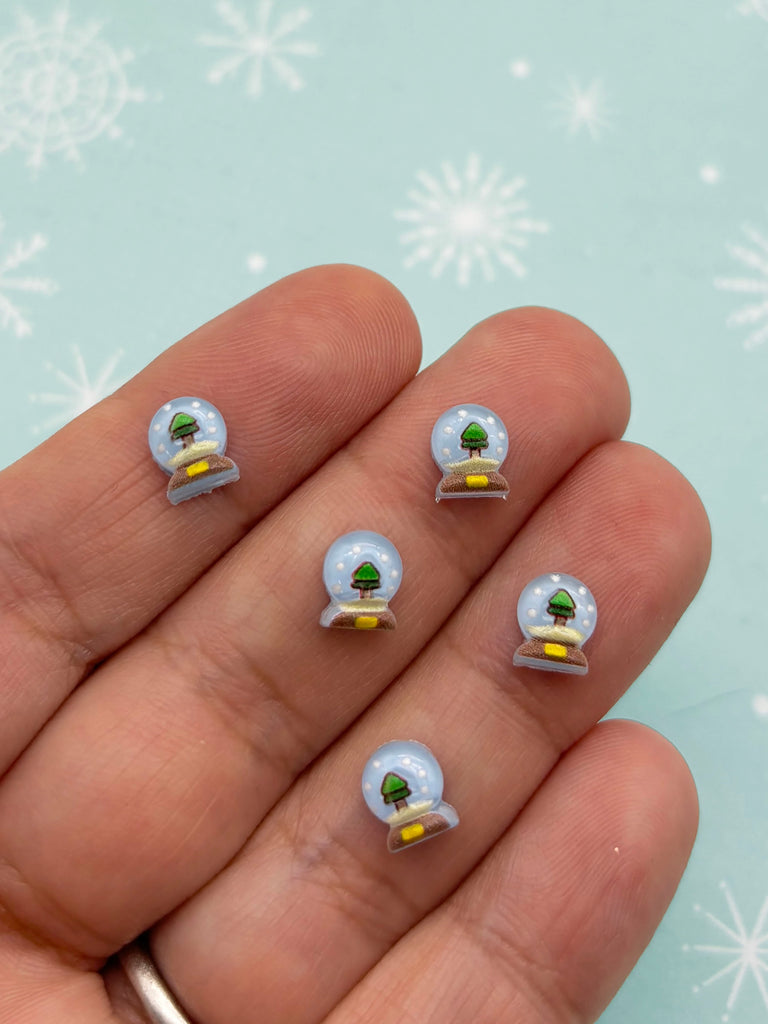 a person's hand holding a snow globe with a green tree on it