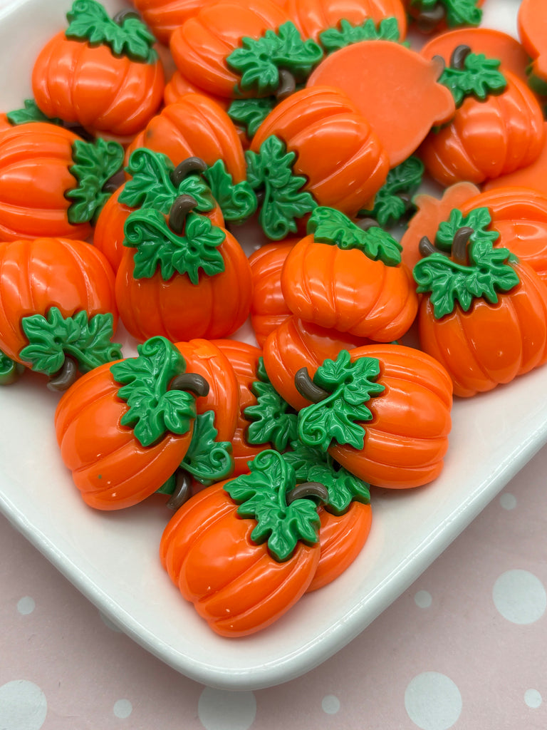 a white plate filled with orange plastic pumpkins, each adorned with green leaves. The pumpkins are arranged in a visually appealing manner, creating a festive and autumnal atmosphere.