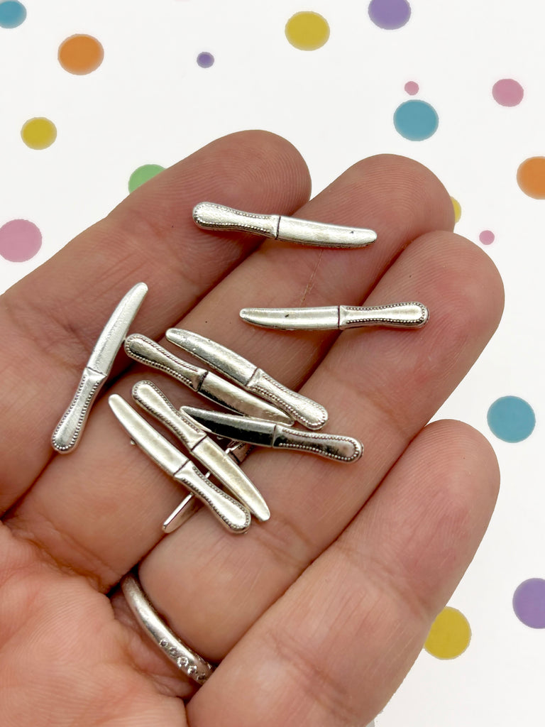 A hand holding a collection of small silver-colored knife blades against a background with colorful polka dots.