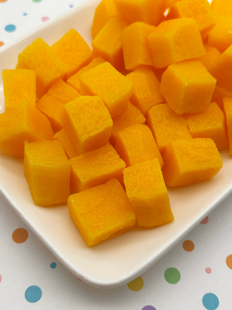 A white plate filled with cubes of bright yellow fruit, likely mangoes, arranged in a visually appealing manner.