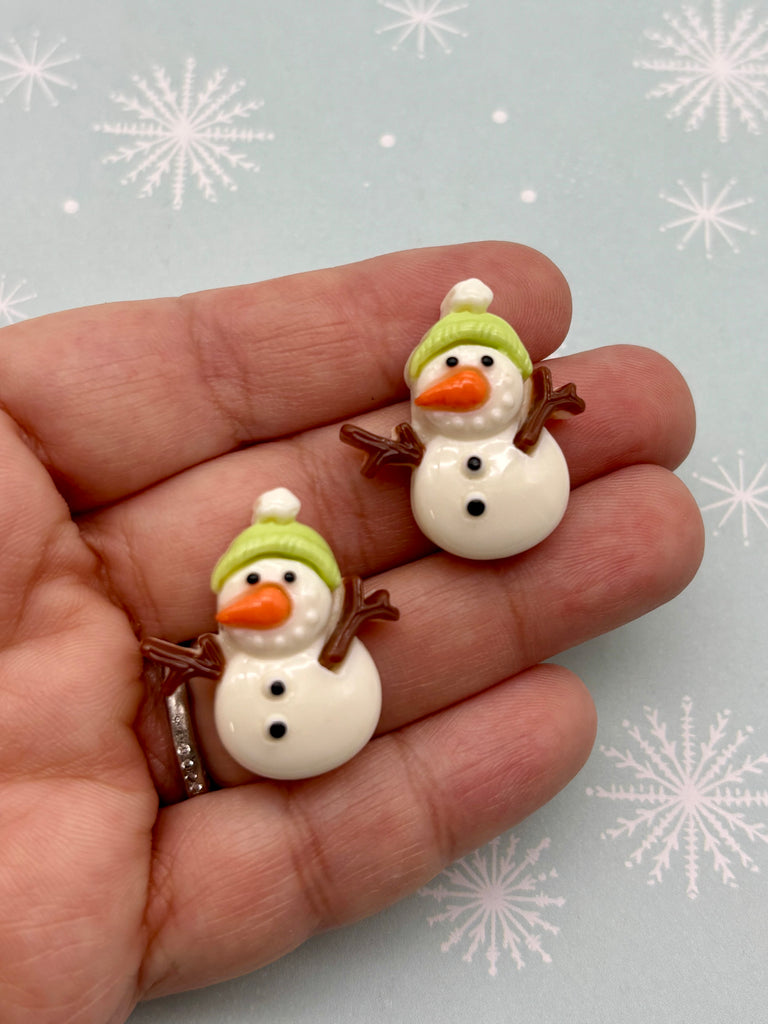 A hand holding two small snowman figurines against a background with snowflakes.