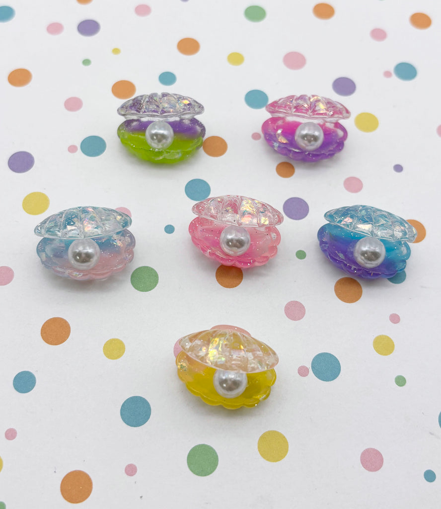 six colorful plastic shells with pearls attached, arranged on a polka dot background.