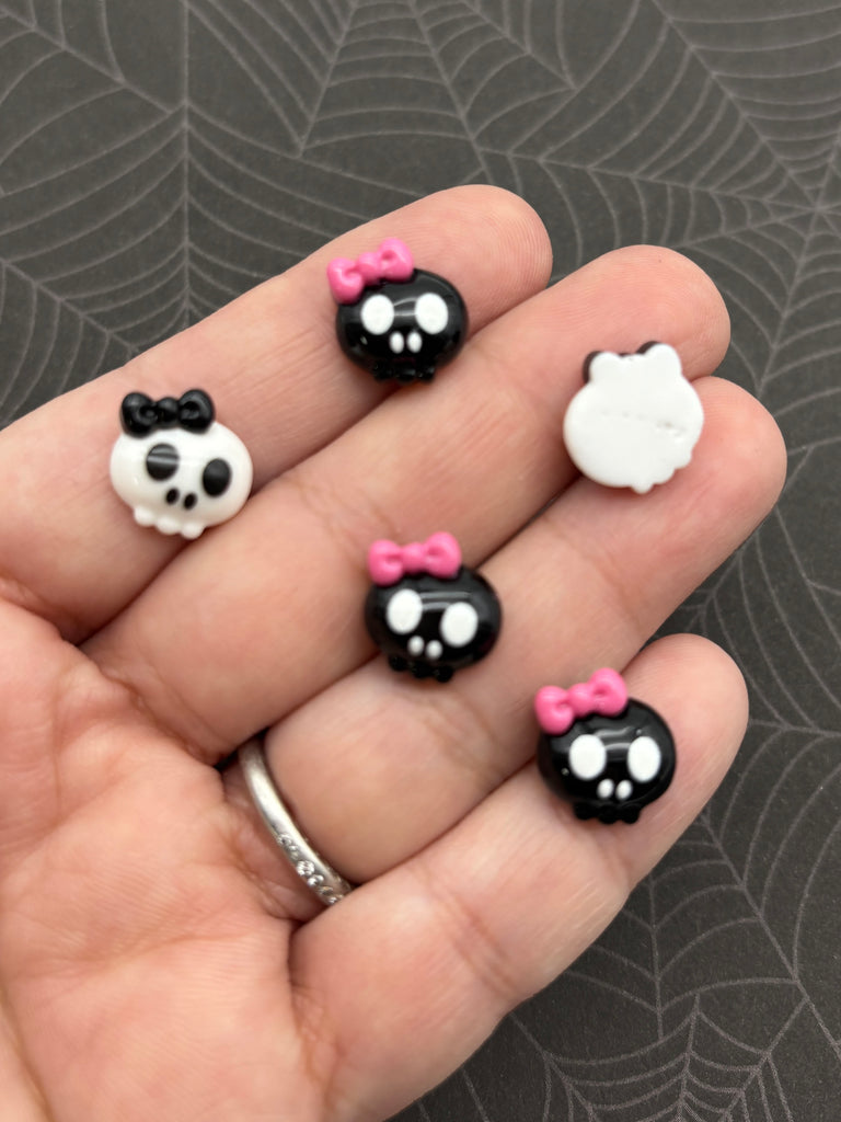 A hand holding five small skull-shaped charms with pink bows on them.