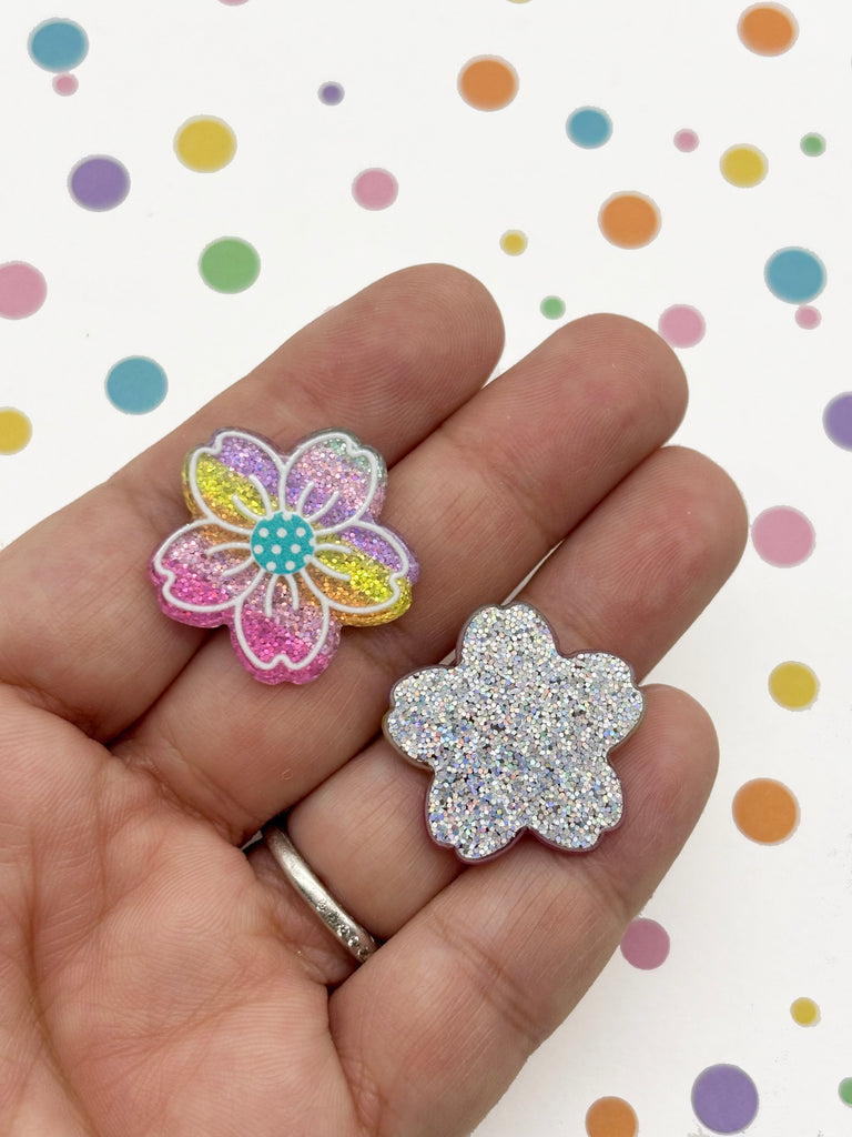 A hand holding two small, glittery flower-shaped objects against a background with colorful polka dots.
