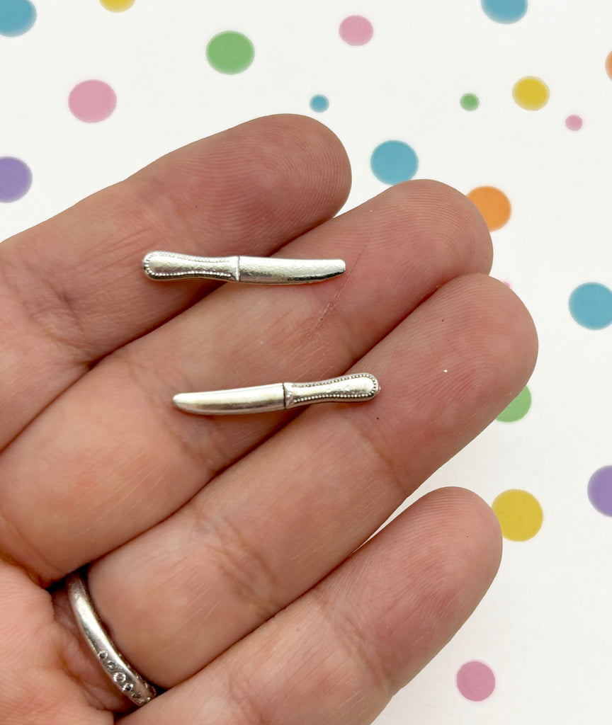 A hand holding two small silver knife blades against a background with colorful polka dots.