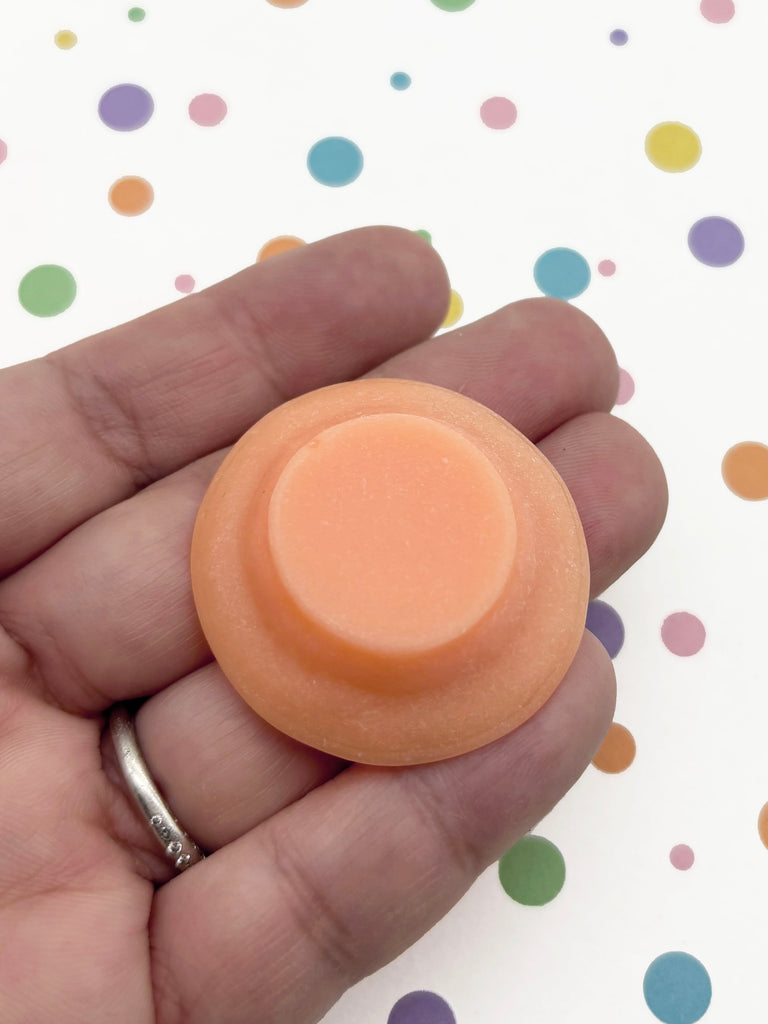 A hand holding a small, round orange object against a background with colorful polka dots.