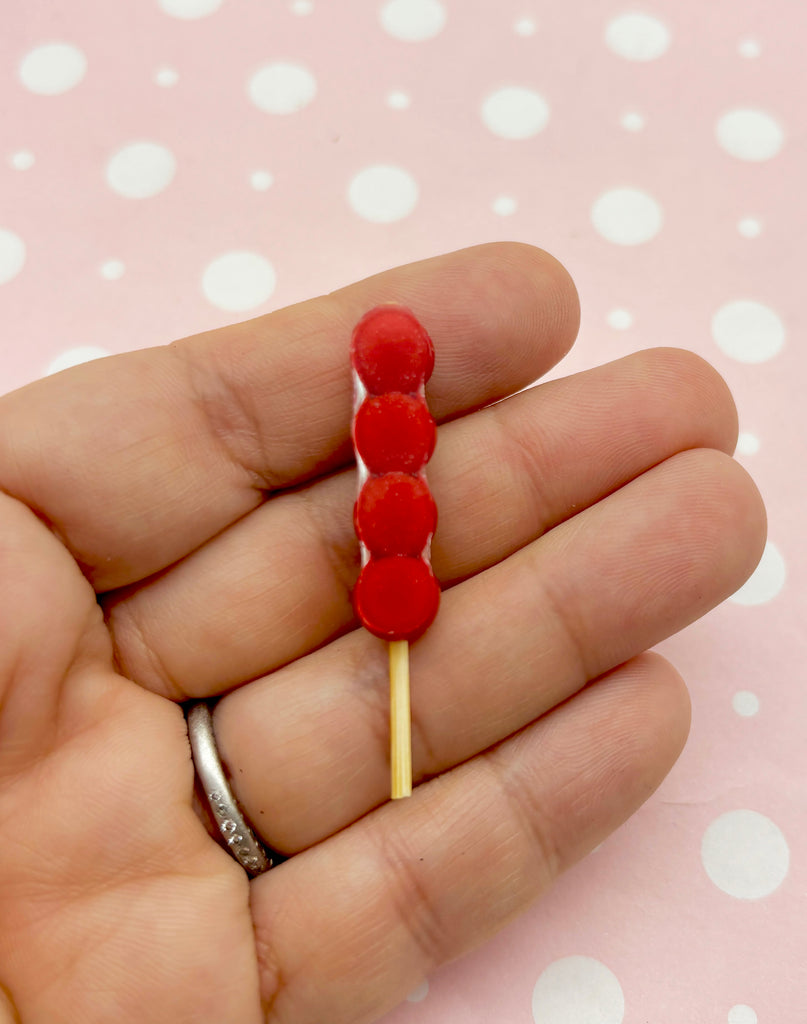 a person is holding a red candy lollipop on a stick