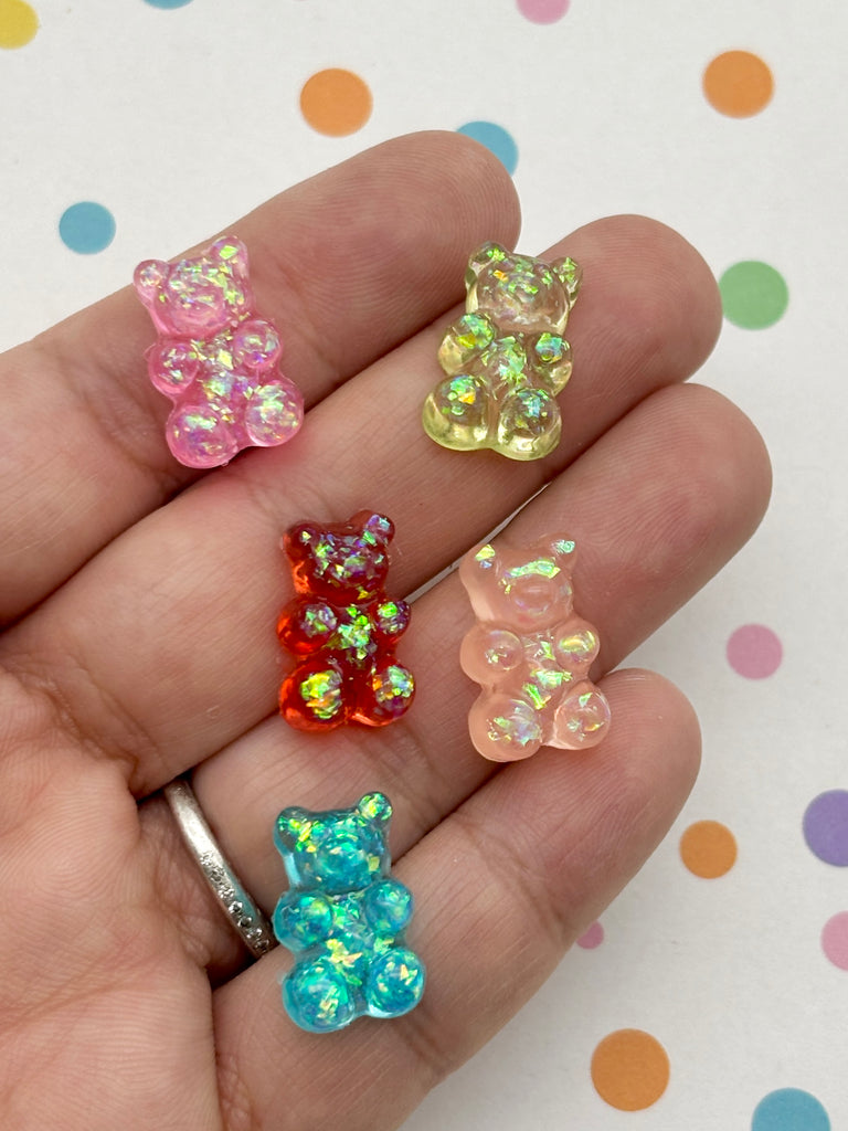 A hand holding a collection of colorful, glittery gummy bear-shaped charms against a background with polka dots.