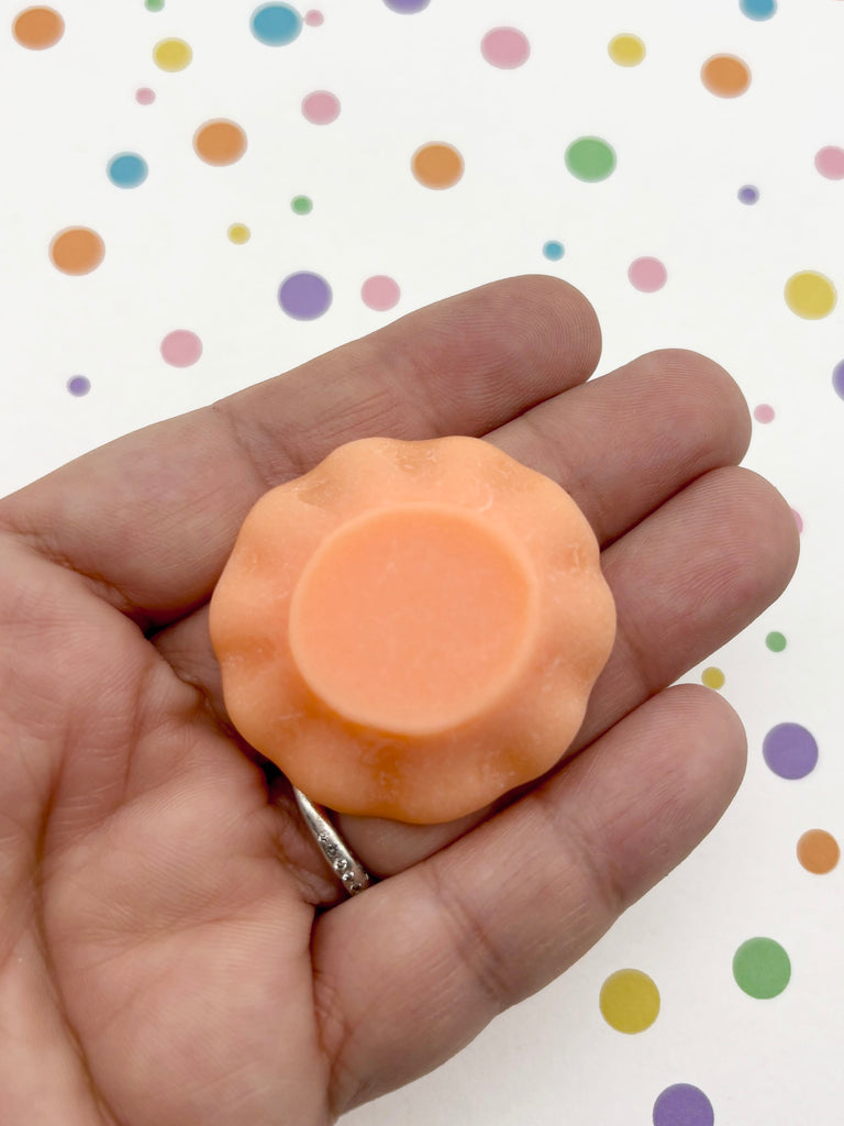 A hand holding a small orange-colored object against a background of colorful polka dots.
