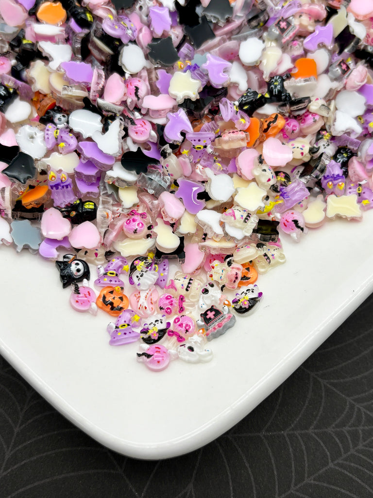 A white plate filled with a variety of colorful, small, and whimsical Halloween-themed stickers, including bats, skulls, and other spooky or festive elements.