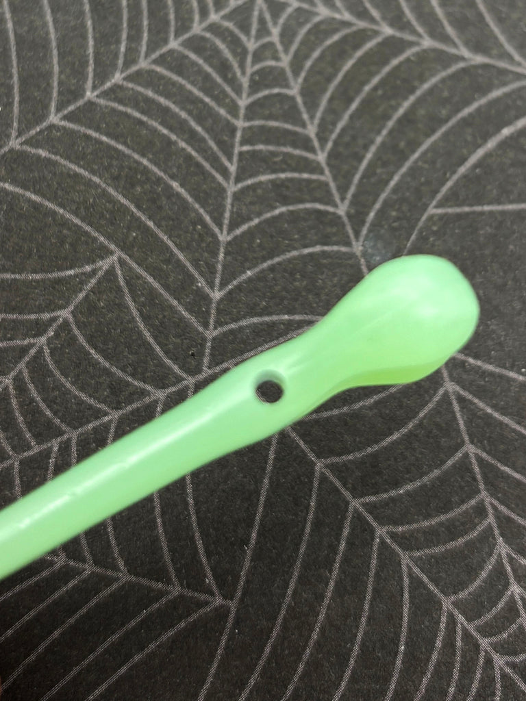 A green plastic spoon with a hole in it is resting on a spider web patterned surface.