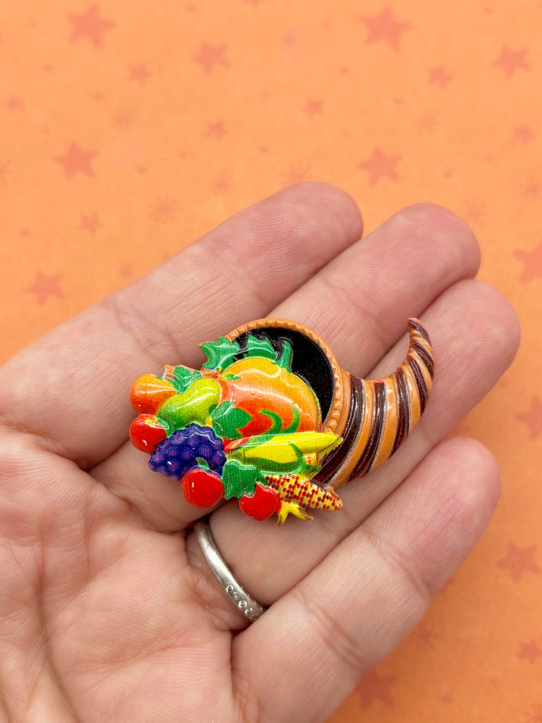 A hand holding a colorful, decorative cornucopia with various fruits and vegetables.