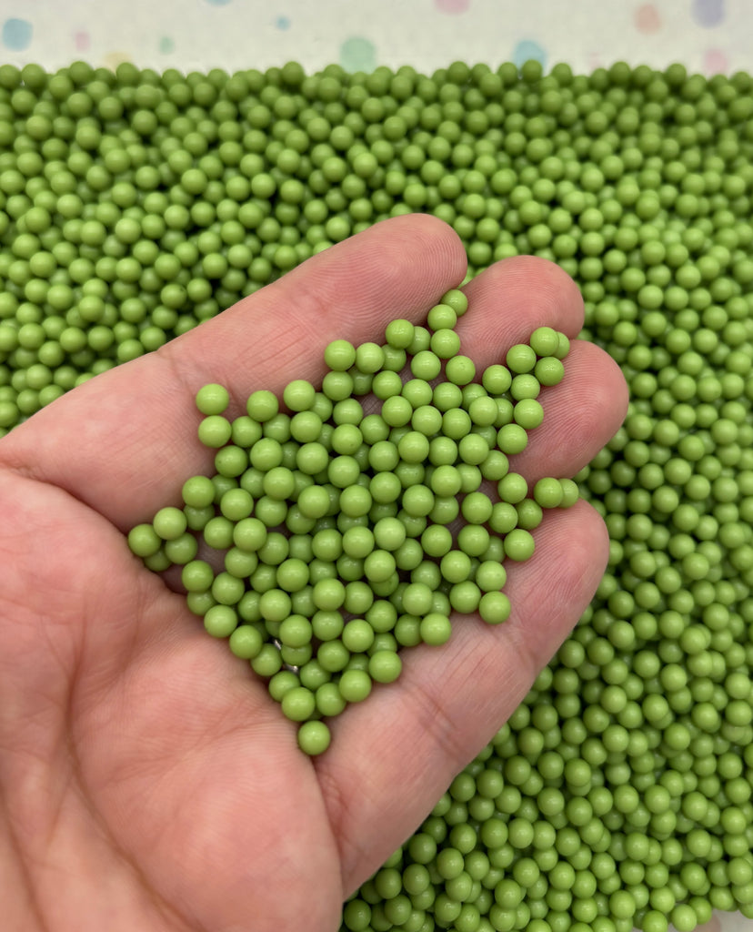 A hand holding a pile of green beads or spheres.