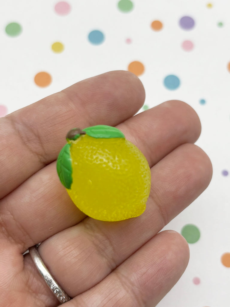 A hand holding a small, yellow, plastic lemon-shaped object with green leaves.