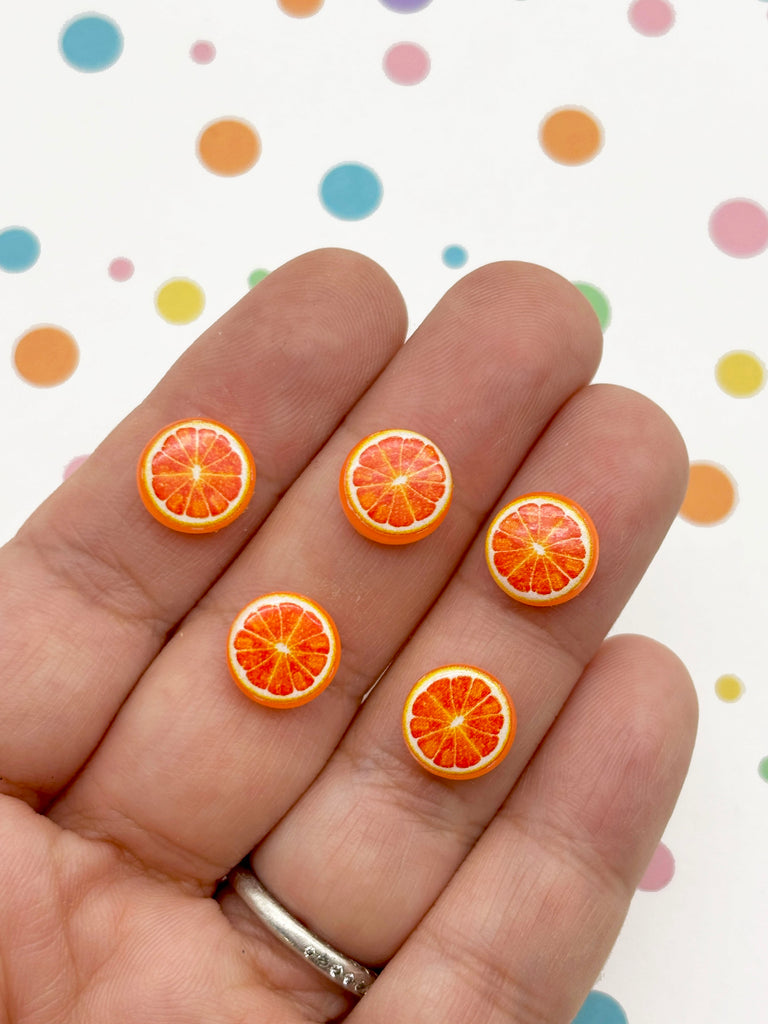 A hand holding five small orange fruit-shaped buttons against a background with colorful polka dots.