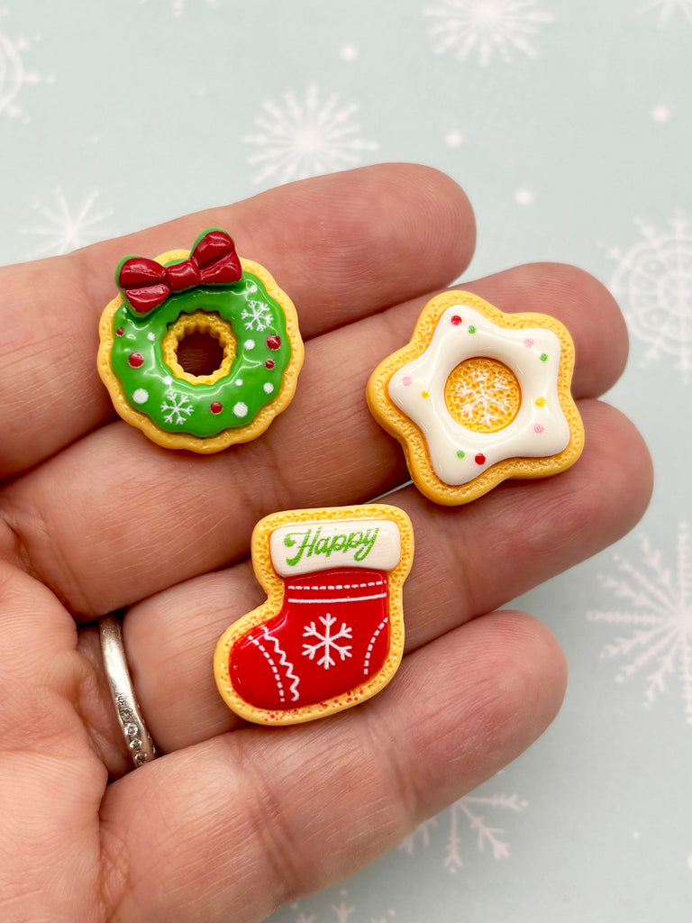 A hand holding three small, festive-themed cookies against a snowy background.