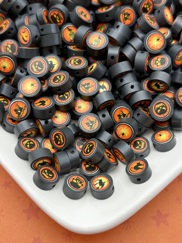 a large pile of black beads with Halloween-themed designs, including jack-o-lanterns and bats, scattered on a white surface.