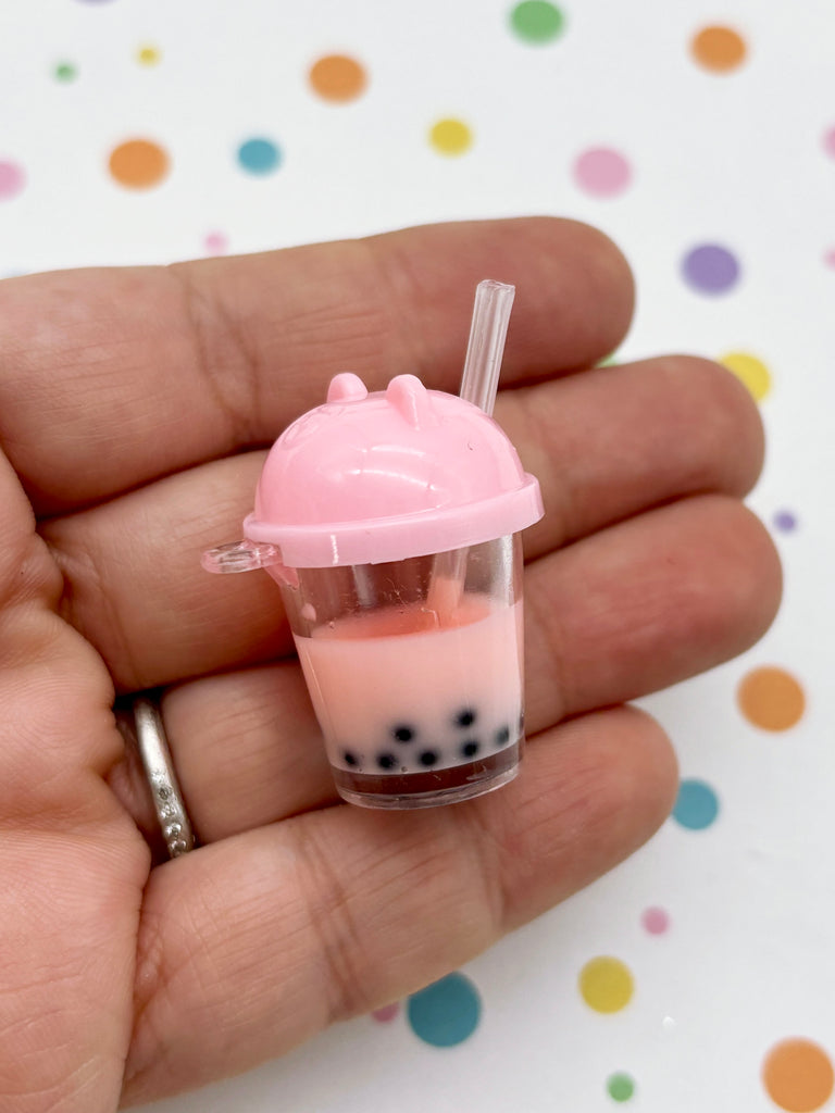 A hand holding a small, pink cup with a straw and a drink inside, against a background with colorful polka dots.