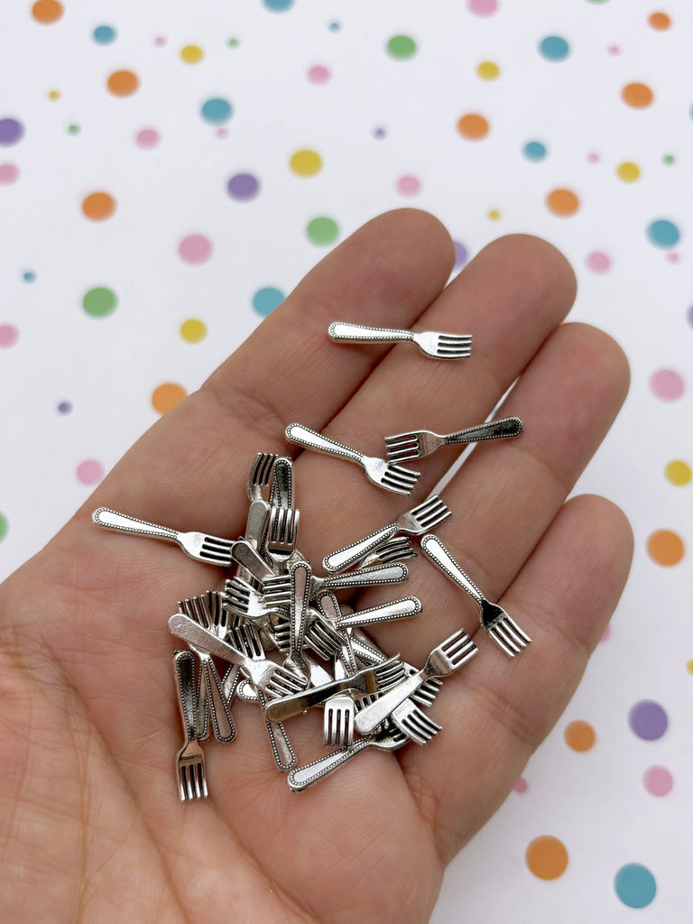 A hand holding a pile of small silver forks against a background with colorful polka dots.