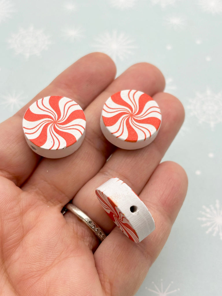 a hand holding a pair of red and white candy cane buttons