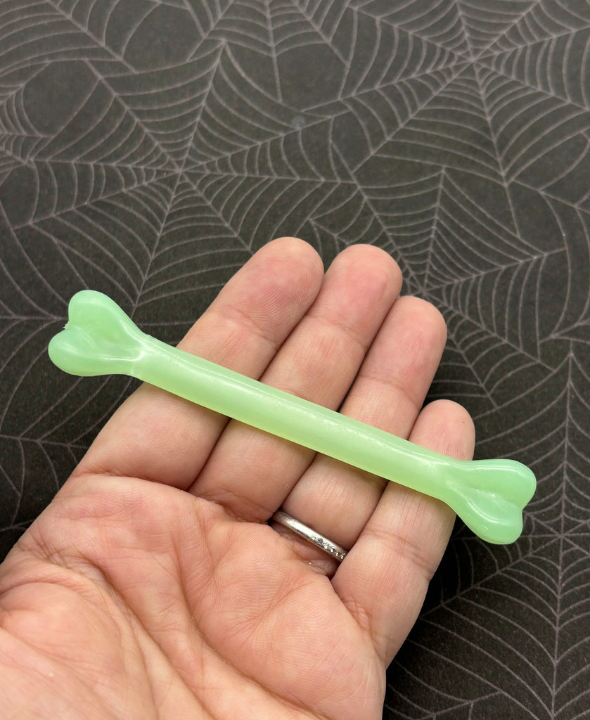A hand holding a green, heart-shaped toothbrush against a spider web background.