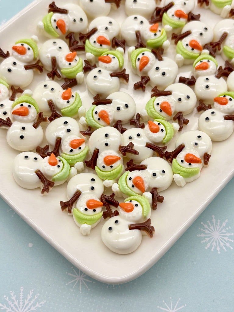 A white plate filled with numerous small snowman figurines made of white and brown materials, arranged in a visually appealing manner.