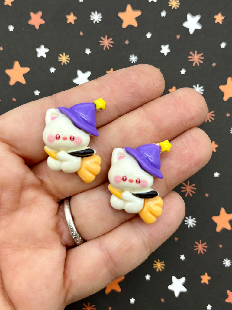 a hand holding a pair of small white and yellow cat earrings