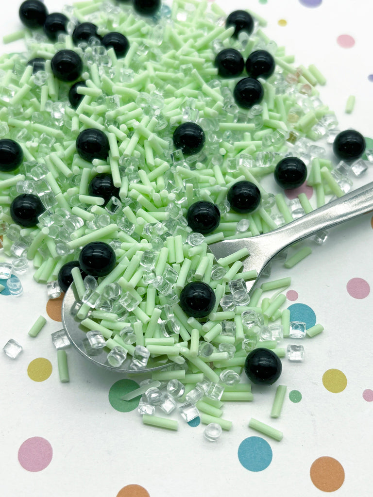 a spoon filled with green sprinkles and black buttons