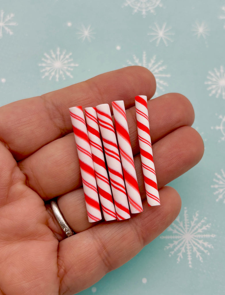 A hand holding a small group of red and white striped candy canes against a background with snowflakes.