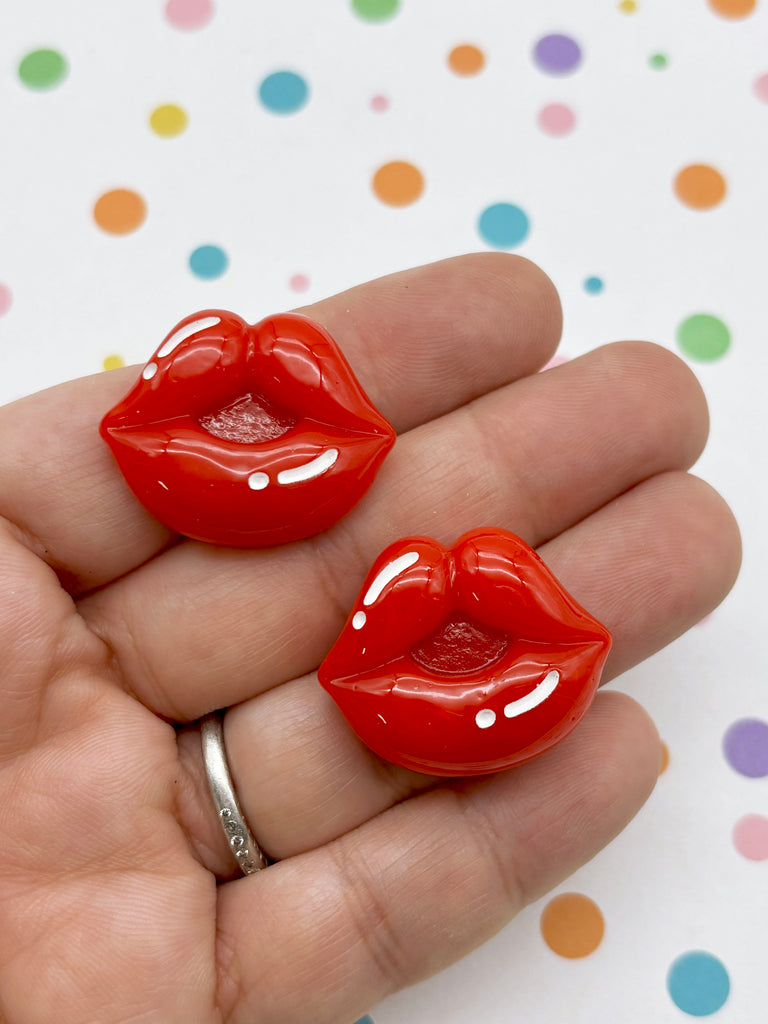 A hand holding two red plastic lips against a background with colorful polka dots.