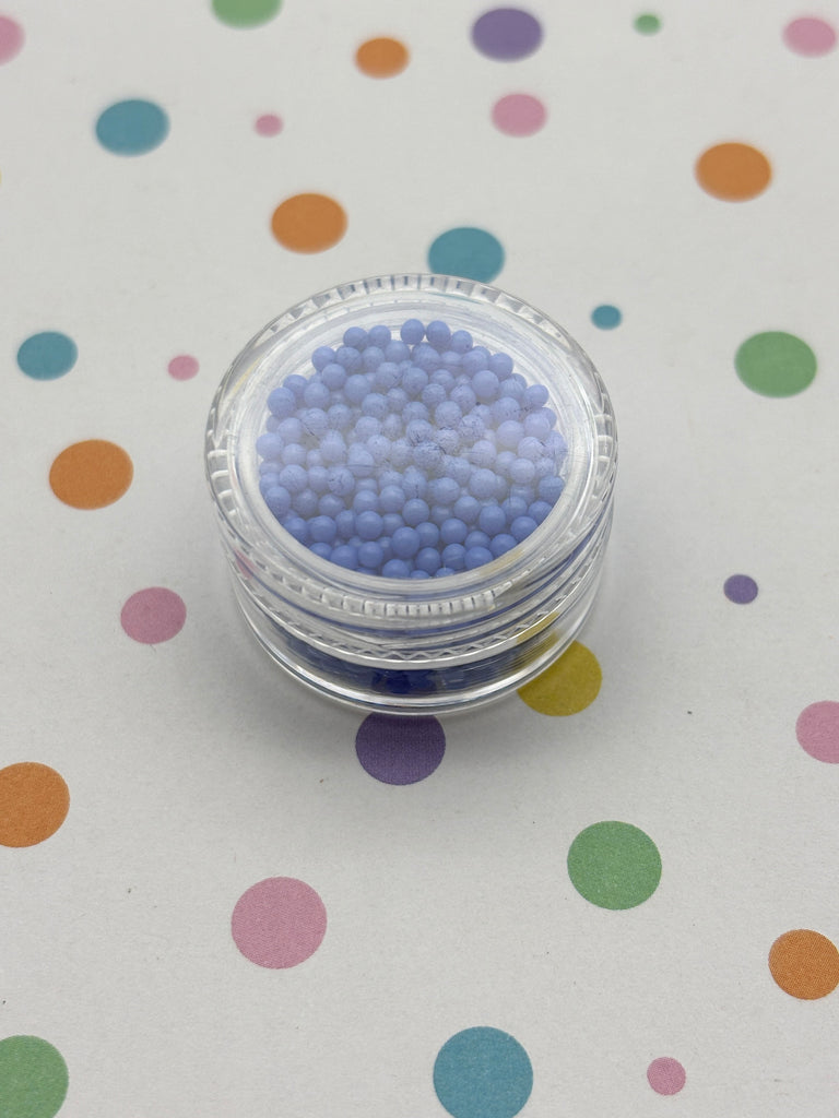 A clear glass jar filled with small, round blue beads is placed on a surface with colorful polka dots.