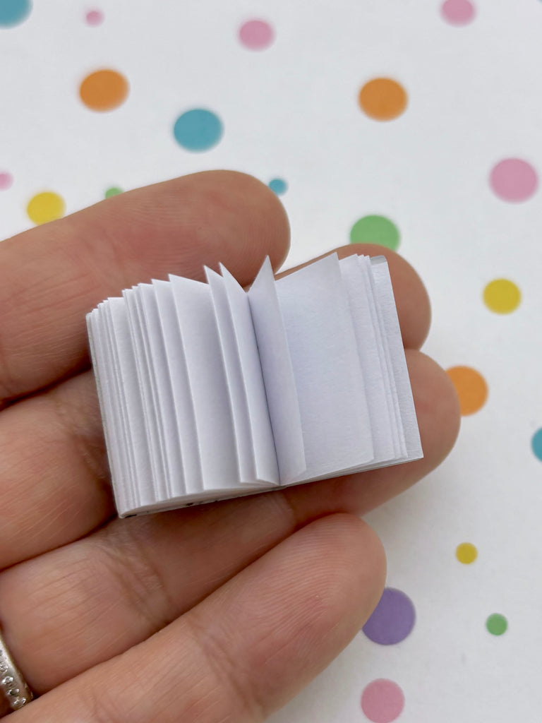 A hand holding a small, open book against a background with colorful polka dots.