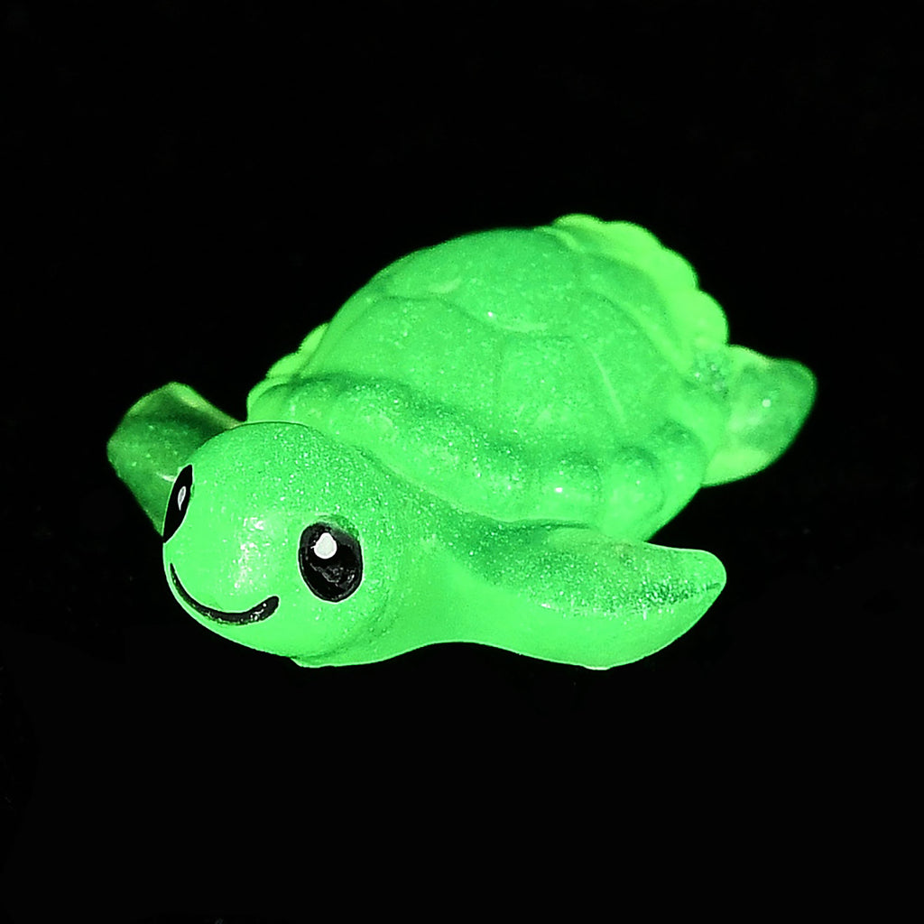 A green, glowing toy turtle is shown against a black background.