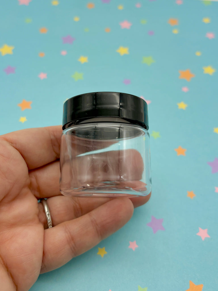 a hand holding a small glass jar with a black lid