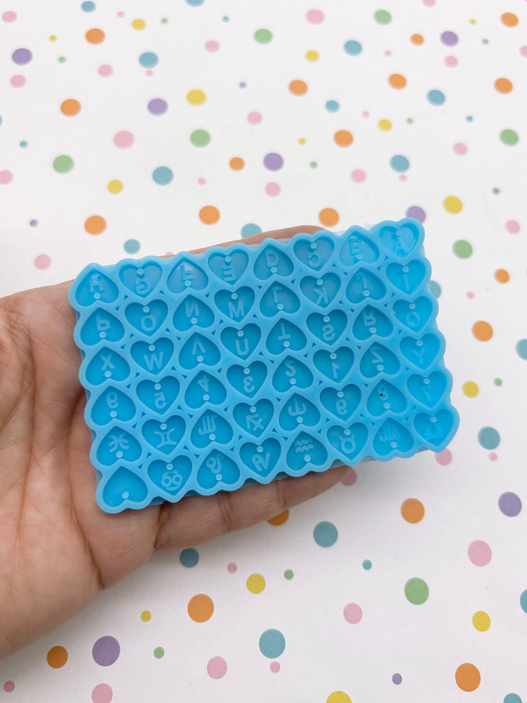 A hand is holding a blue heart-shaped mold with the word "LOVE" written on it against a background with colorful polka dots.