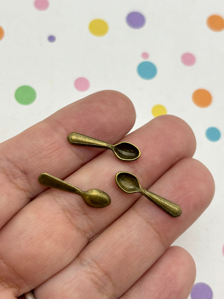 A hand holding three small brass spoons against a background with colorful polka dots.