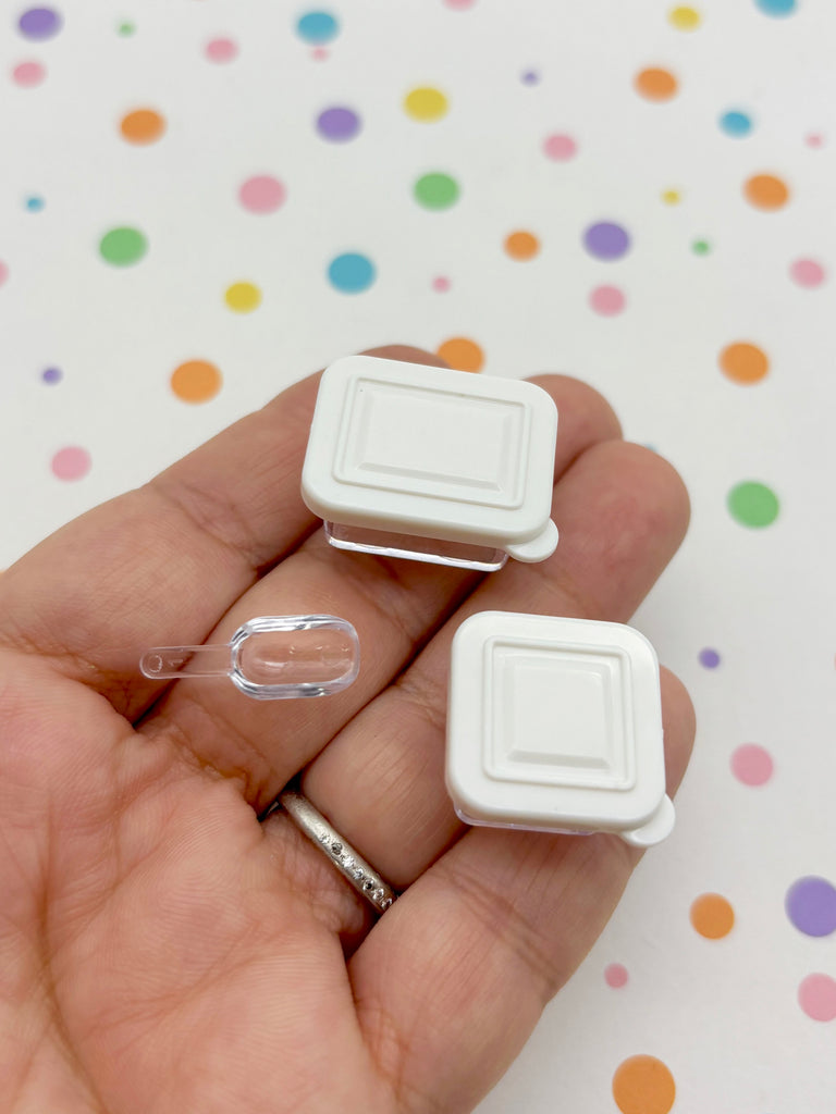 A hand holding two small white plastic containers with clear plastic lids, against a background with colorful polka dots.