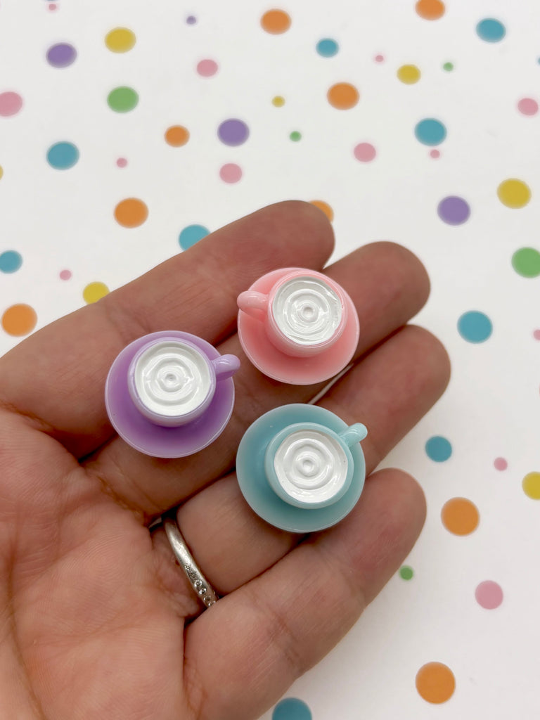 A hand holding three small, colorful plastic cups against a background with multicolored polka dots.