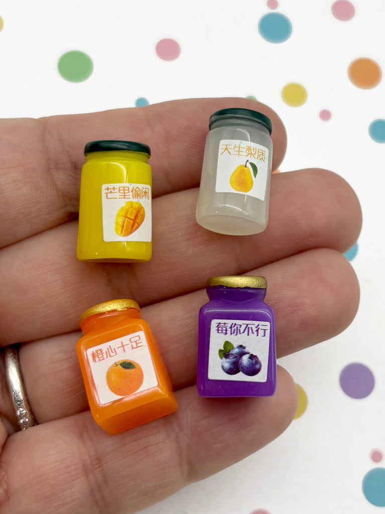 A hand holding four small jars of jam, each with a different flavor and label.