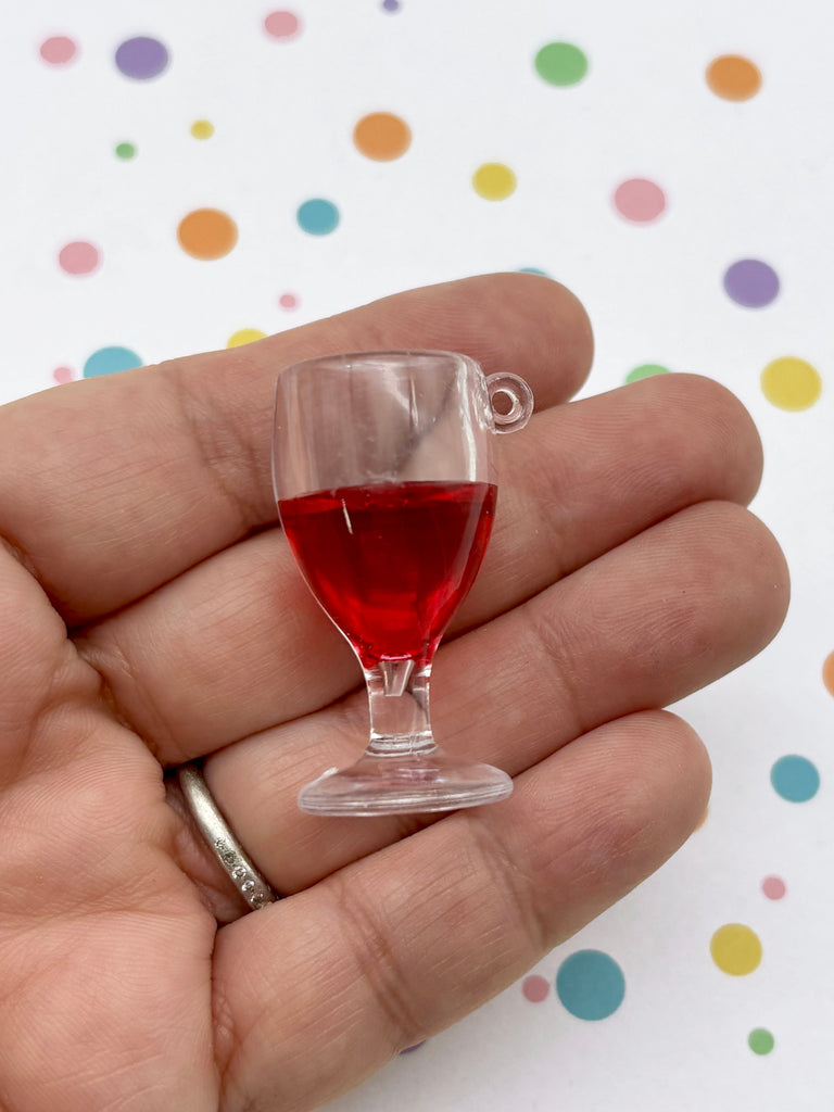 A hand holding a small glass of red liquid against a background with colorful polka dots.