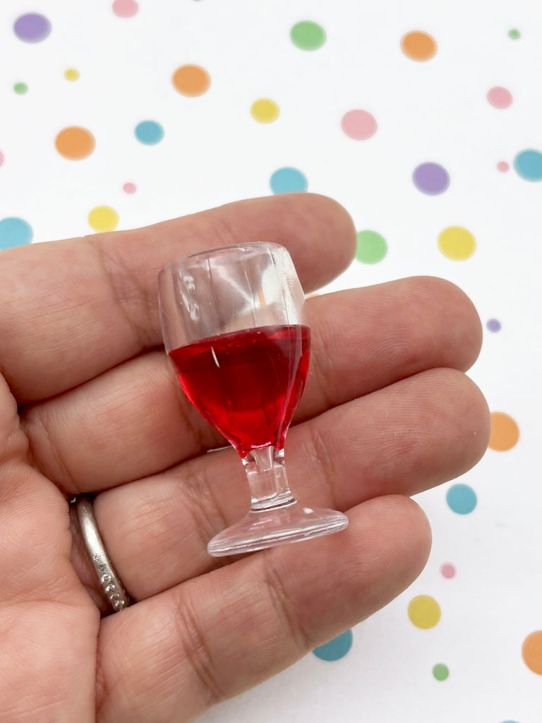 A hand holding a small glass filled with red liquid against a background of colorful polka dots.