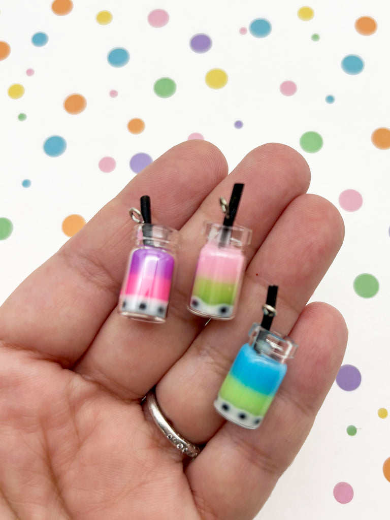 A hand holding three small, colorful pendants shaped like drinks against a background with multicolored polka dots.