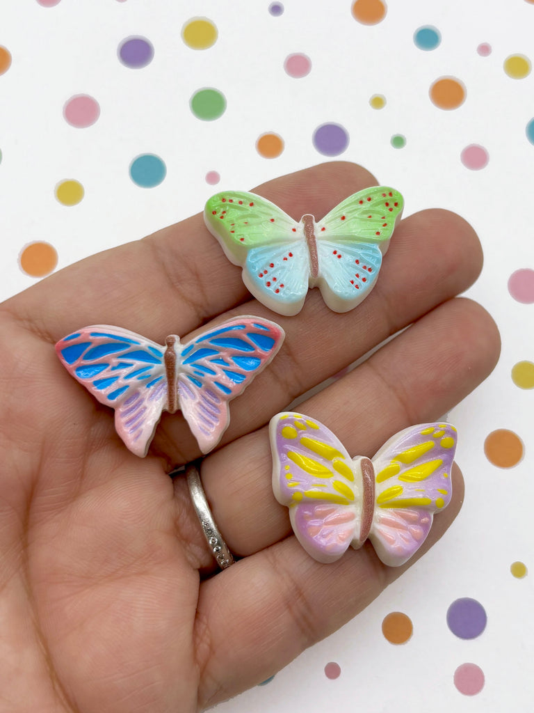 A hand holding three colorful butterfly-shaped objects against a background with polka dots.