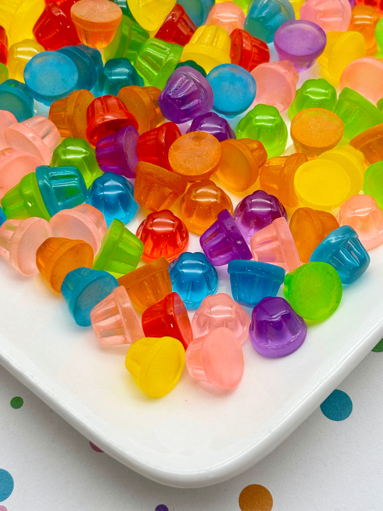 A plate filled with a variety of colorful jelly beans, including red, orange, yellow, green, blue, and purple, scattered across a white surface.