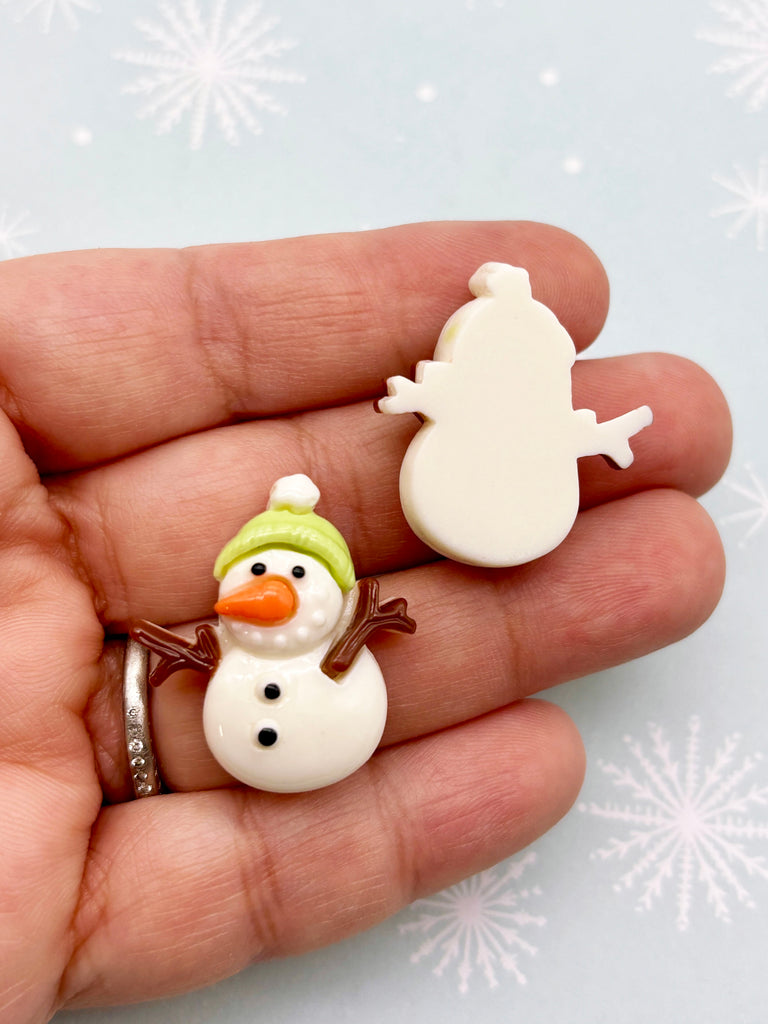A hand holding a small snowman figurine against a background with snowflakes.